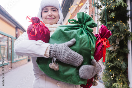 Smiling woman carrying gift bags at street in Christmas photo