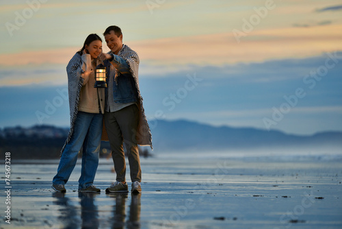Smiling couple with lantern standing on beach at sunset photo