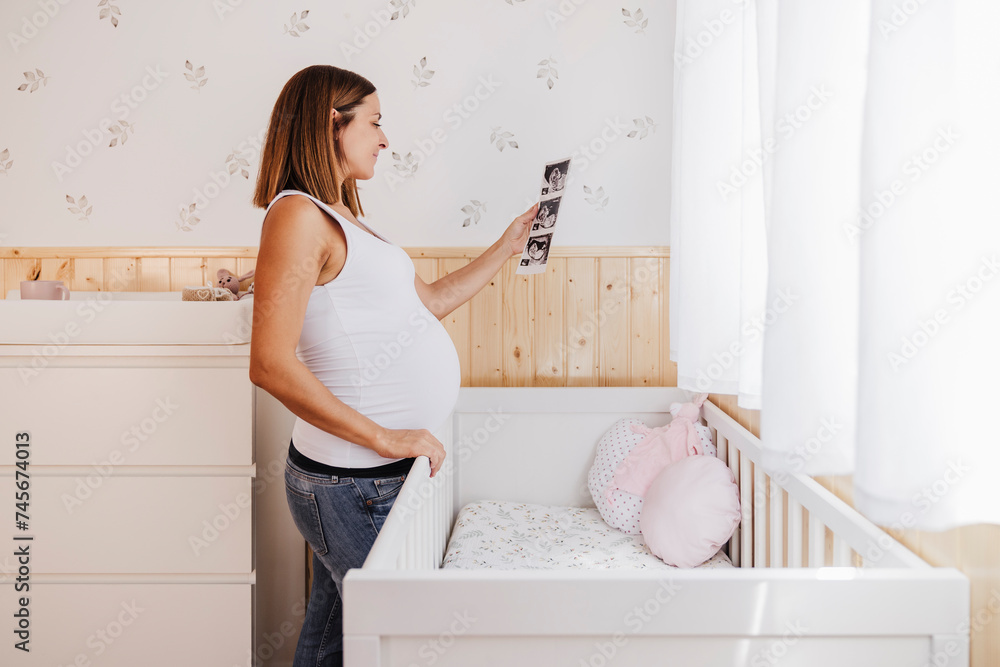 Pregnant woman holding ultrasound photograph by crib at home Pregnant woman holding ultrasound photograph by crib at home