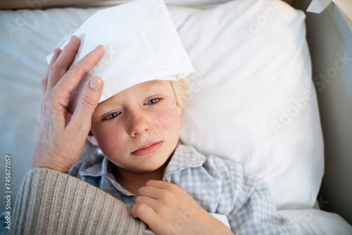 Thoughtful sick boy with white compress on forehead at home photo