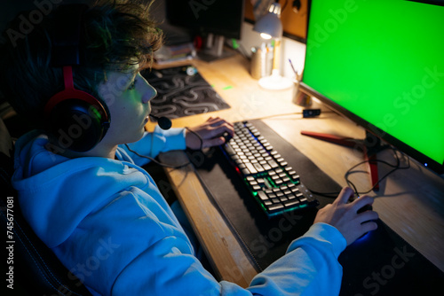Boy wearing headset and playing video game on computer at home photo