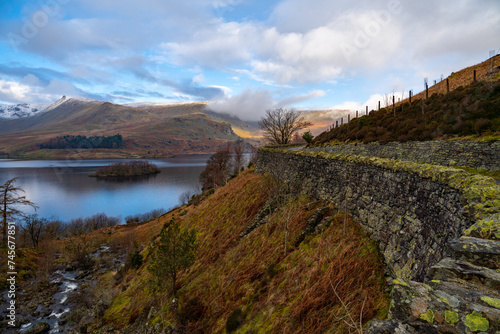 Haweswater reservoir featuring a mossy wall on the small lakeside road looking toward kidsy pike a mountain in the background and the little island. Photo taken in the Lake District, Cumbria, England