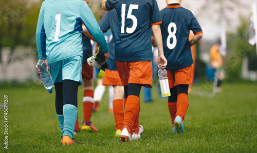 Fototapeta Naklejka Na Ścianę i Meble -  Young boys in the sports team walk off the grass pitch holding bottles of water in their hands after losing the game. Kids in blue soccer jerseys. Male elementary school sports team