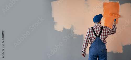 painter man at work with a paint roller painting wall in orange colour. Home renovation concept. Banner. photo