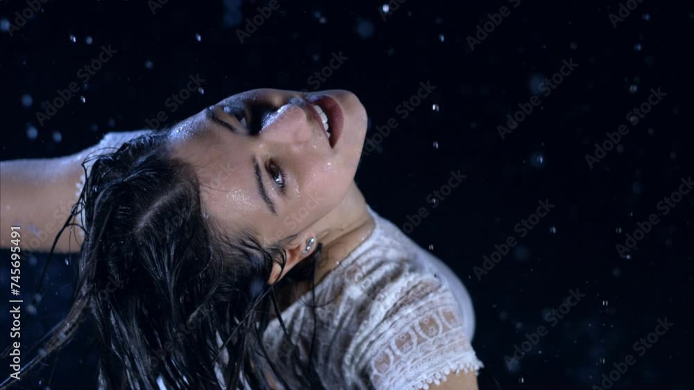 Super slow motion of young carefree happy wet brunette woman in white dress with open arms is having fun and enjoy rain drops falling on her in hot summer day at night. Super slow motion of young carefree happy wet brunette woman in white dress with open arms is having fun and enjoy rain drops falling on her in hot summer day at night.