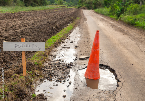 Pothole, deep pothole filled with rainwater, with orange traffic cone and sign to the left pointing to the pothole on rural, single track road in East Yorkshire.  Horizontal.  Copy space