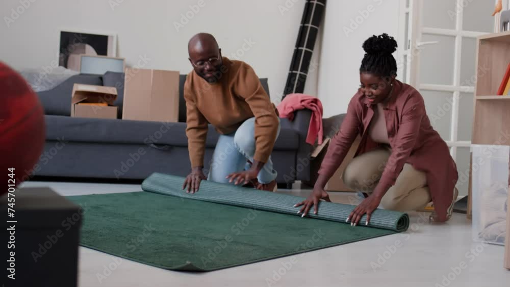 African American family couple rolling carpet together in living room while preparing for moving in new home African American family couple rolling carpet together in living room while preparing for moving in new home