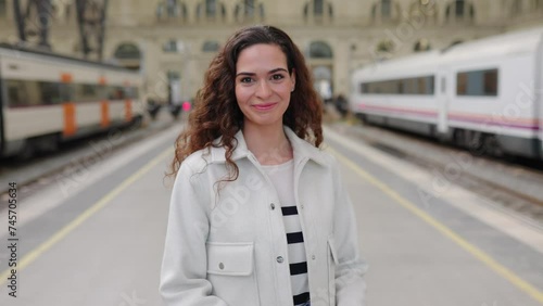 Smiling portrait of young beautiful woman in casual clothes looking at camera standing at train station platform.