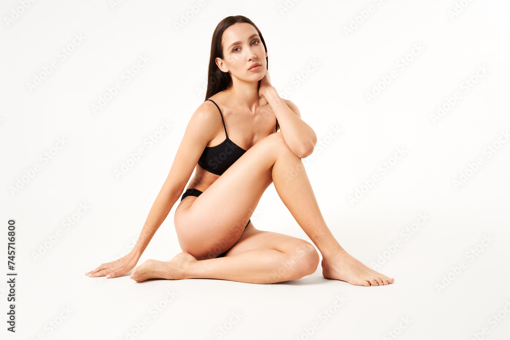 Young beautiful woman with perfect body in black underwear sitting on floor posing on studio Young beautiful woman with perfect body in black underwear sitting on floor posing on studio