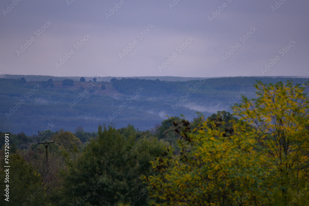 Evening landscape with fog rising above the green forest that will change in the autumn season