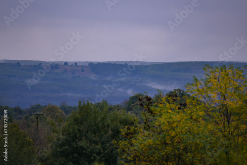 Evening landscape with fog rising above the green forest that will change in the autumn season