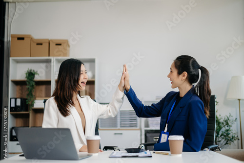 Female discussing new project with Female colleague. Young women talking with young Asian man in office.