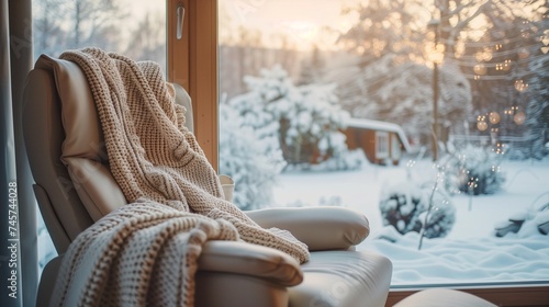 A cozy recliner chair by a window overlooking a snowy landscape, with a warm knitted blanket.