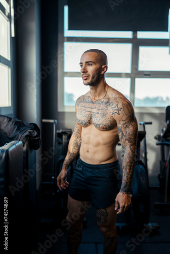 Chico joven tatuado y musculoso posando en gimnasio sin camiseta y con ropa moderna © MiguelAngelJunquera