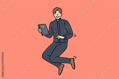 Joyful catholic priest jumps up with bible in hands, inviting you to temple for sunday worship. Happy priest man in religious clothes holding book with christian cross and looking at screen smiling