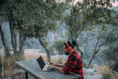 A young man is working on a laptop at a camping site in the mountains.