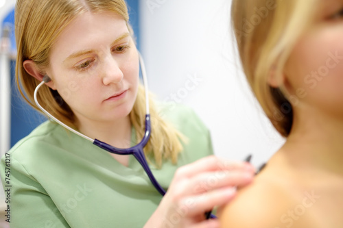 Caring female doctor with stethoscope listening to heartbeat and breathing of young girl. Schoolgirl patient is at pediatrician appointment. Treatment of viral and infectious diseases photo