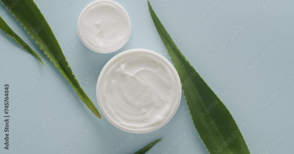 Top view on spinning open jar with cream for face and aloe vera leaves on blue background. Beauty and skin care concept. Advertising of natural moisturizer Top view on spinning open jar with cream for face and aloe vera leaves on blue background. Beauty and skin care concept. Advertising of natural moisturizer