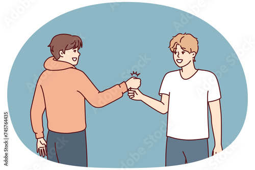 Two young guys bump their fists when they meet, making greeting to members of student fraternity. Positive teenage boys in casual clothes say goodbye after fun together walk
