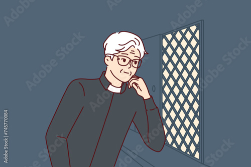 Man catholic priest listens to confession, located in church in room with mesh wall. Elderly christian minister conducts confession procedure, allowing parishioners to remove burden from souls