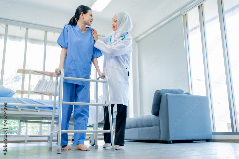 Fototapeta premium Healthcare, A Muslim Female doctor help a patient who is doing physical therapy and is practicing walking with a walking stick in the hospital.