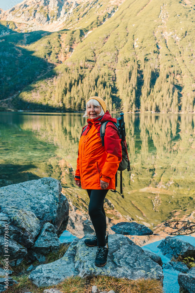 Lady tourist with a backpack standing on top of the mountain and enjoy the beautiful view of mountains Morskie Oko lake. Hiking travel and adventure in Poland, Tatry  - obrazy, fototapety, plakaty 