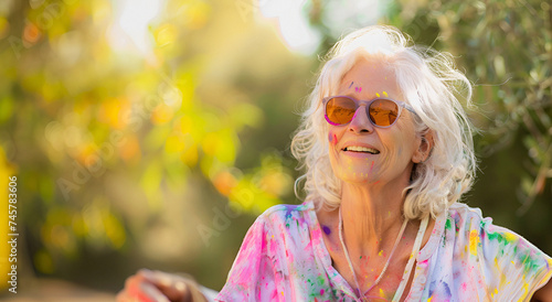 Bright elderly lady with glasses immersed in a colorful Holi celebration. Perfect image for advertising cultural events and holidays. Copy space.