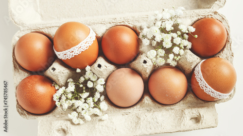 Brown Easter eggs decorated lace and white gypsophila flowers in carton on white background. Easter celebration concept. Top view photo of festive food of painted chicken egg retro toned photo