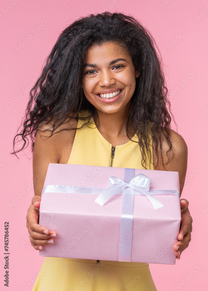 Vertical portrait of happy smiling beautiful birthday girl posing with decorated present box in hands over pastel pink background Vertical portrait of happy smiling beautiful birthday girl posing with decorated present box in hands over pastel pink background