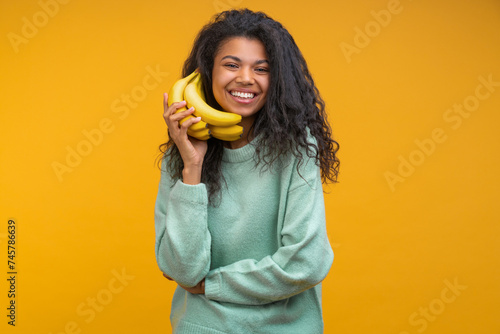 Studio portrait of funny positive casually dressed girl pretending to make a call via banana phone isolated over bright colored orange yellow background
