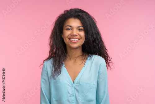 Studio portrait of beautiful casually dressed african american young woman with charming smile posing over pastel pink background