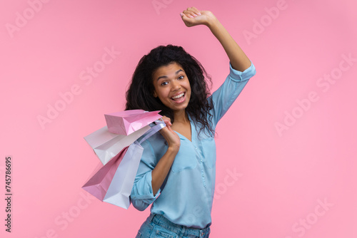 Studio portrait of happy smiling beautiful cheerful young woman with a bunch of paper bags in hand having fun enjoying shopping, isolated over pastel pink background