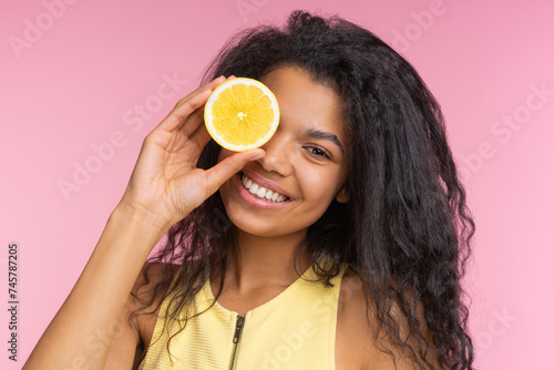 Close up studio portrait of beautiful happy smiling girl posing over pastel pink background with a lemon cut in a half in hand