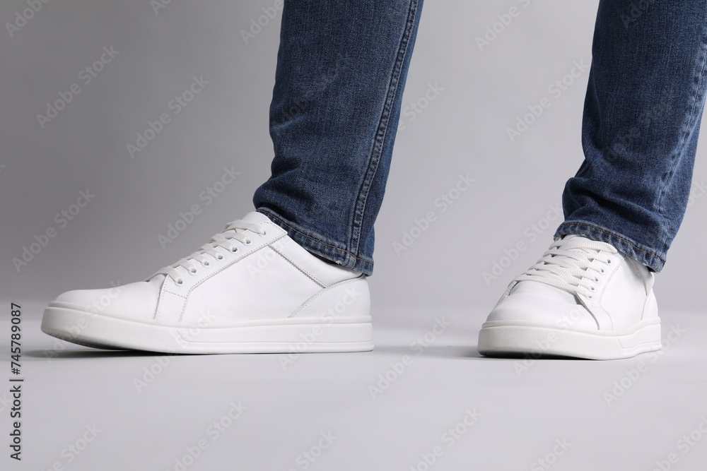 Man wearing stylish white sneakers on grey background, closeup Man wearing stylish white sneakers on grey background, closeup