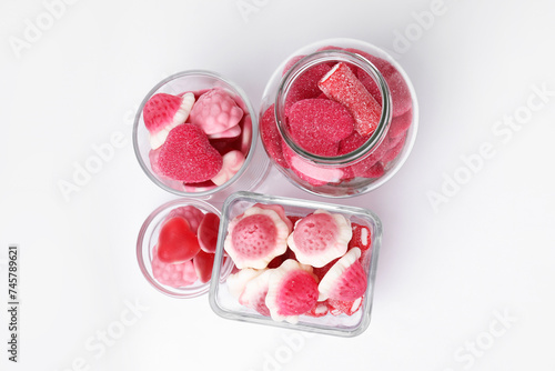 Different yummy pink candies in glass jar and bowls on white background, flat lay