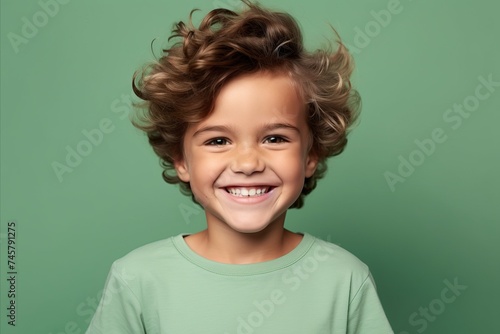 Portrait of cute smiling little boy with curly hair on green background