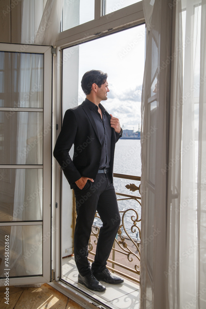 An attractive man in a black classic suit on the balcony.