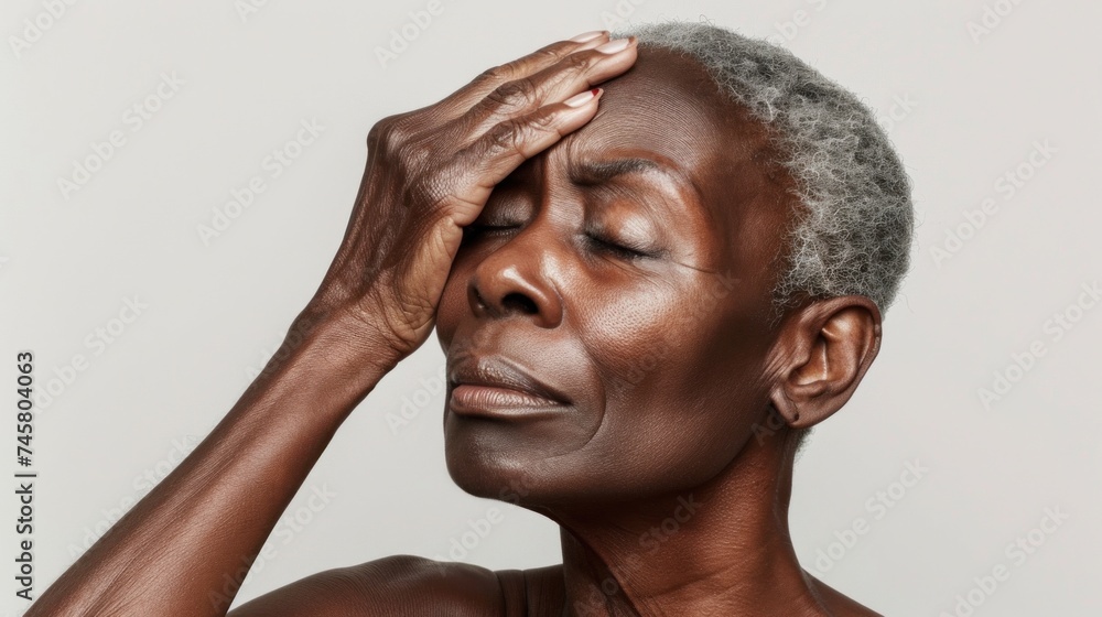 Fototapeta premium A woman with gray hair closed eyes and a hand on her forehead conveying a sense of deep thought or concern.