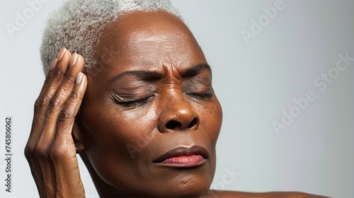 A woman with a short gray hairstyle her eyes closed and her hand on her forehead appearing to be in deep thought or possibly experiencing a headache.