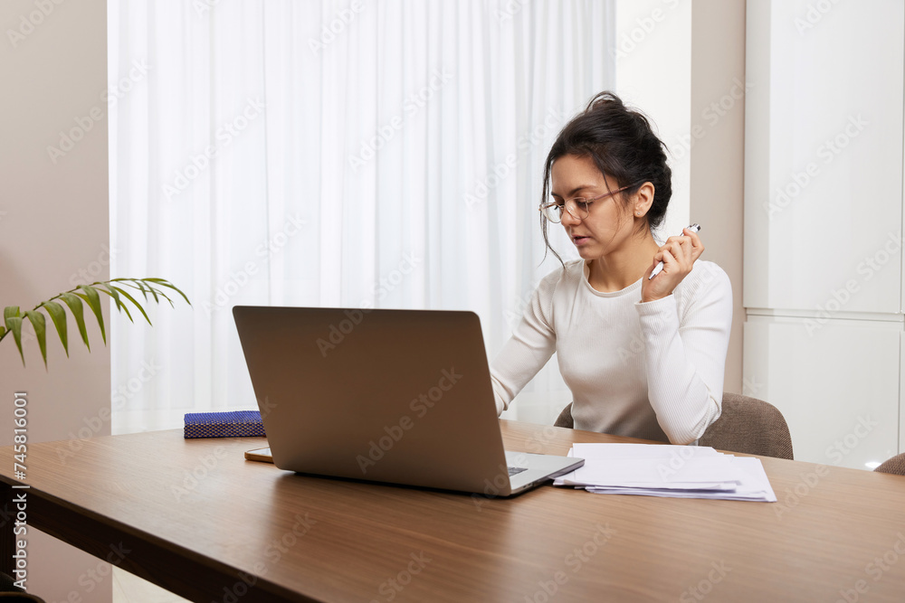 pretty woman in glasses using laptop and communicates with customer on internet at home pretty woman in glasses using laptop and communicates with customer on internet at home