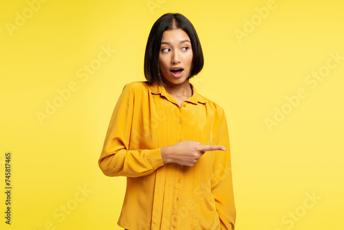 Portrait excited attractive asian woman pointing finger on copy space, isolated on yellow background © speed300