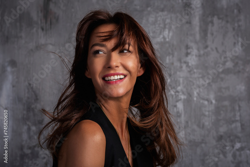 Headshot of beautiful brunette haired woman cheerful smiling at grey wall