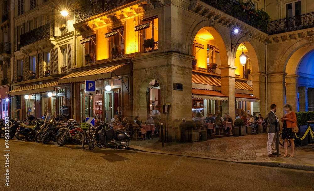 Cozy street with tables of cafe in Paris at night, France. Night cityscape of Paris. Architecture and landmarks of Paris.