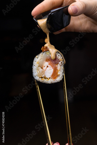 Hands holding chopsticks with a piece of sushi on a black background