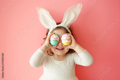 cute little girl with bunny ears holds Easter eggs by the eyes, Easter holiday card with copy space