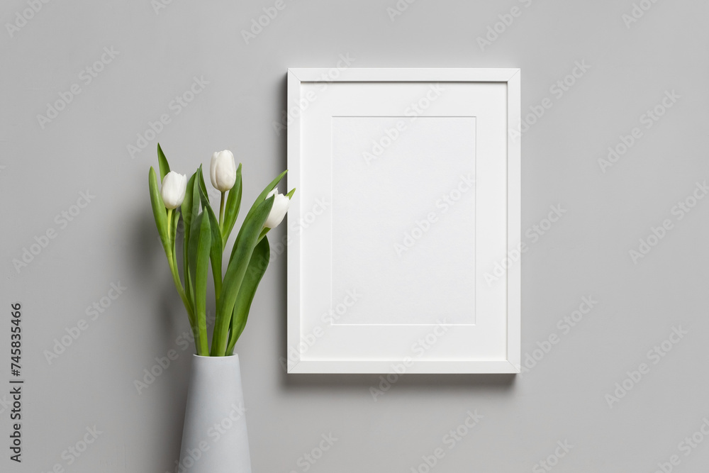 Blank vertical frame mockup with white fresh tulip flower in vase over grey wall background - obrazy, fototapety, plakaty 