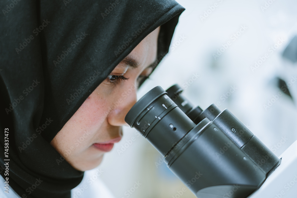 Fototapeta premium Scientist in Hijab Examining Samples with Microscope