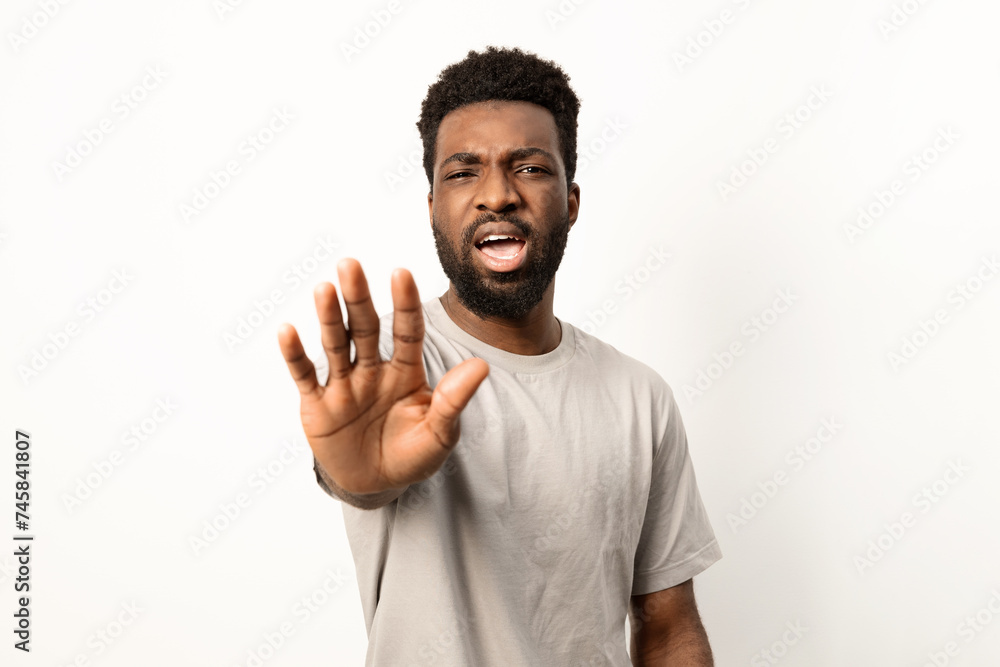 Portrait of an African American man showing a stop hand sign, displaying rejection or warning on a white backdrop. Portrait of an African American man showing a stop hand sign, displaying rejection or warning on a white backdrop.