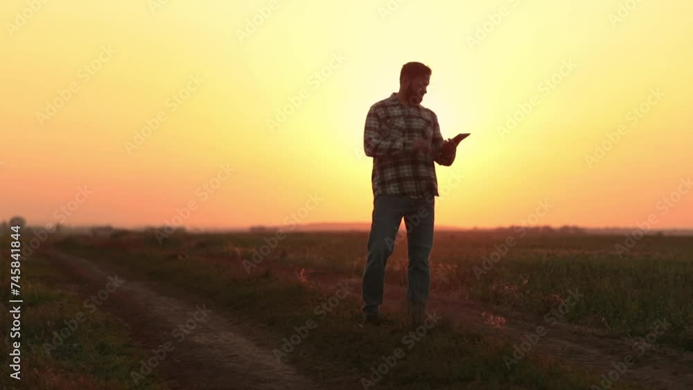 A farmer walks on a freshly mown field with a tablet in his hands and checks the work of his subordinates. Young farmer in the field A farmer walks on a freshly mown field with a tablet in his hands and checks the work of his subordinates. Young farmer in the field