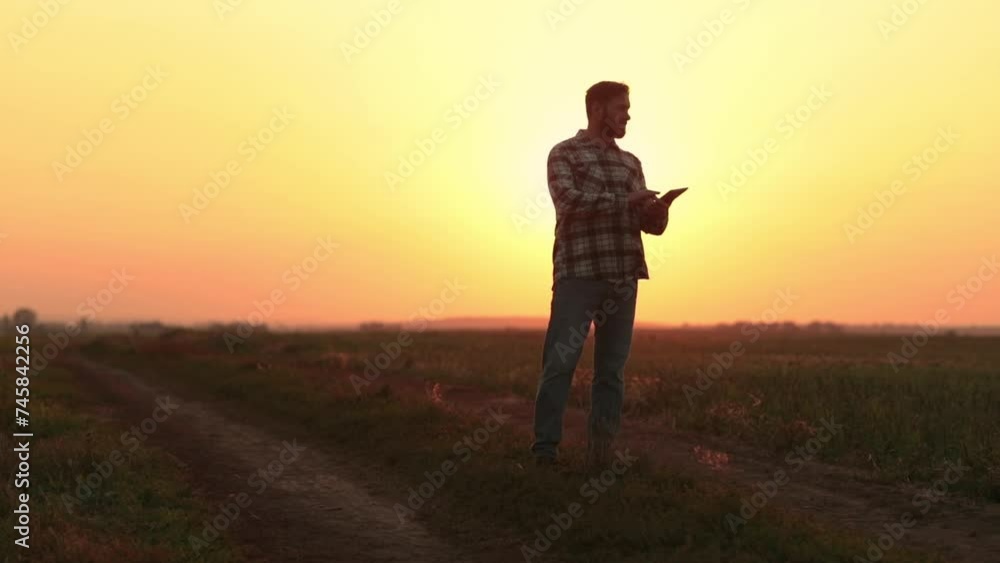 A farmer walks on a freshly mown field with a tablet in his hands and checks the work of his subordinates. Young farmer in the field A farmer walks on a freshly mown field with a tablet in his hands and checks the work of his subordinates. Young farmer in the field